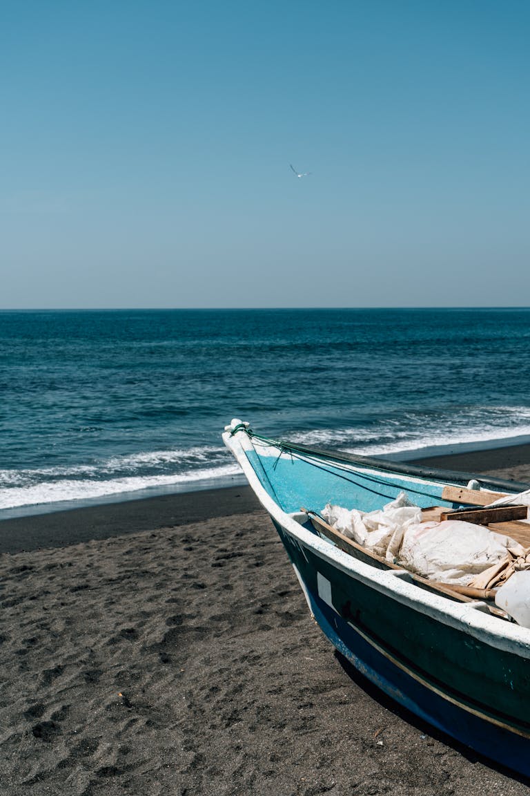 A peaceful beach with a colorful boat resting on the sandy shore under a clear blue sky.