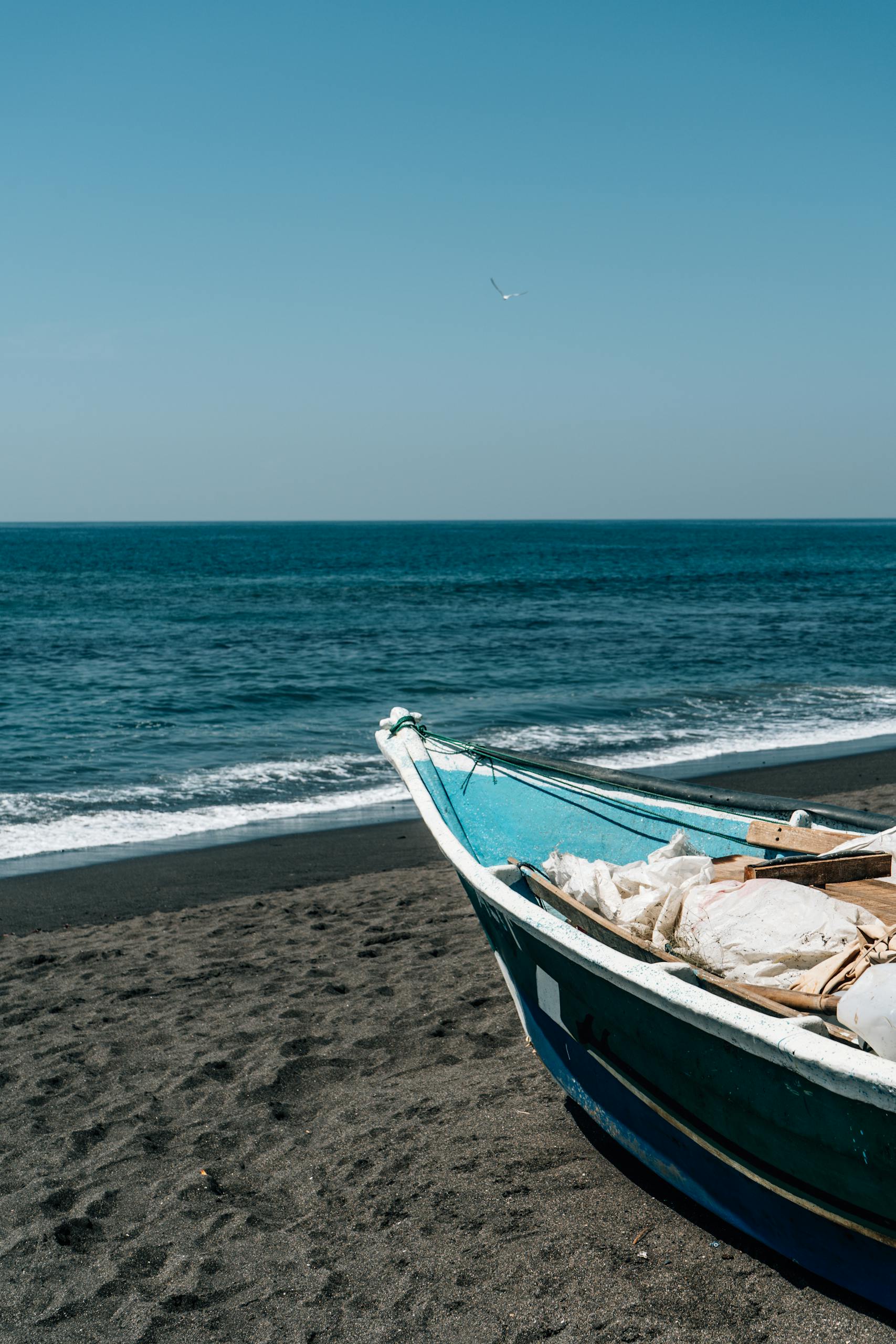 A peaceful beach with a colorful boat resting on the sandy shore under a clear blue sky.